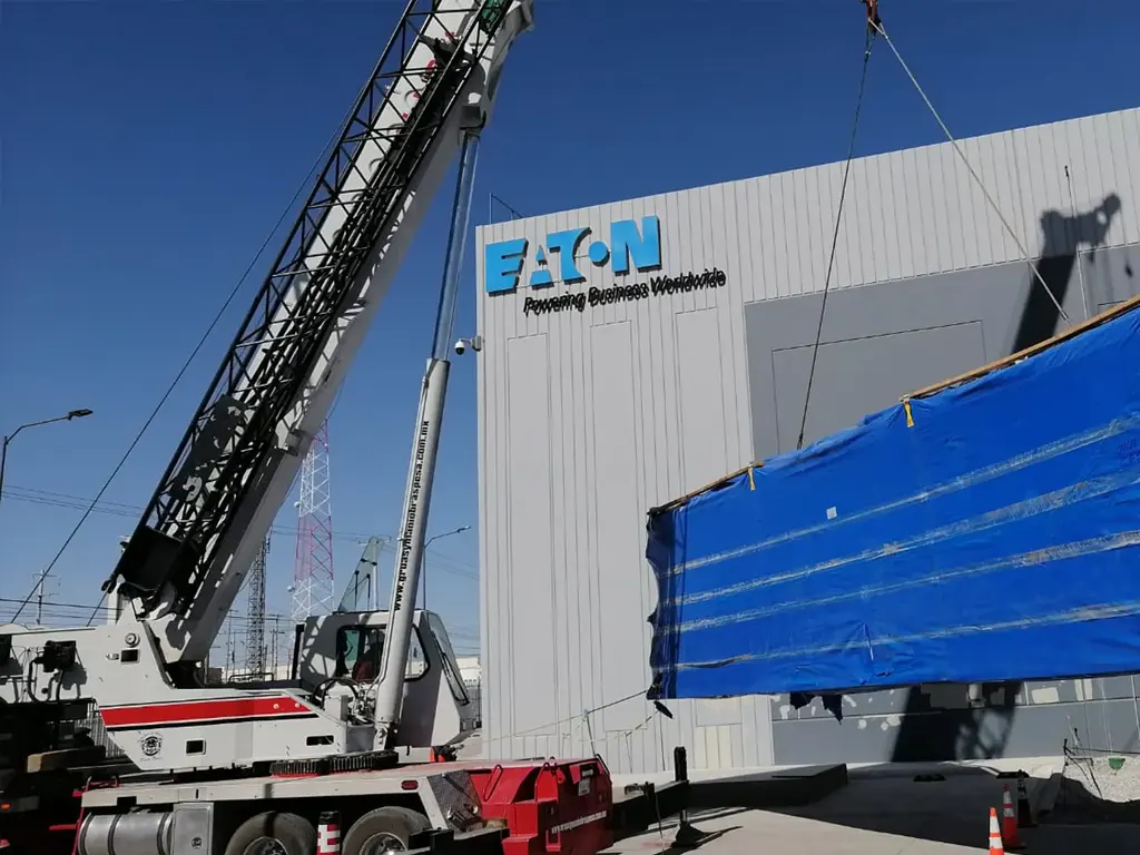 Grúa manipulando contenedor azul con complejo industrial en el fondo